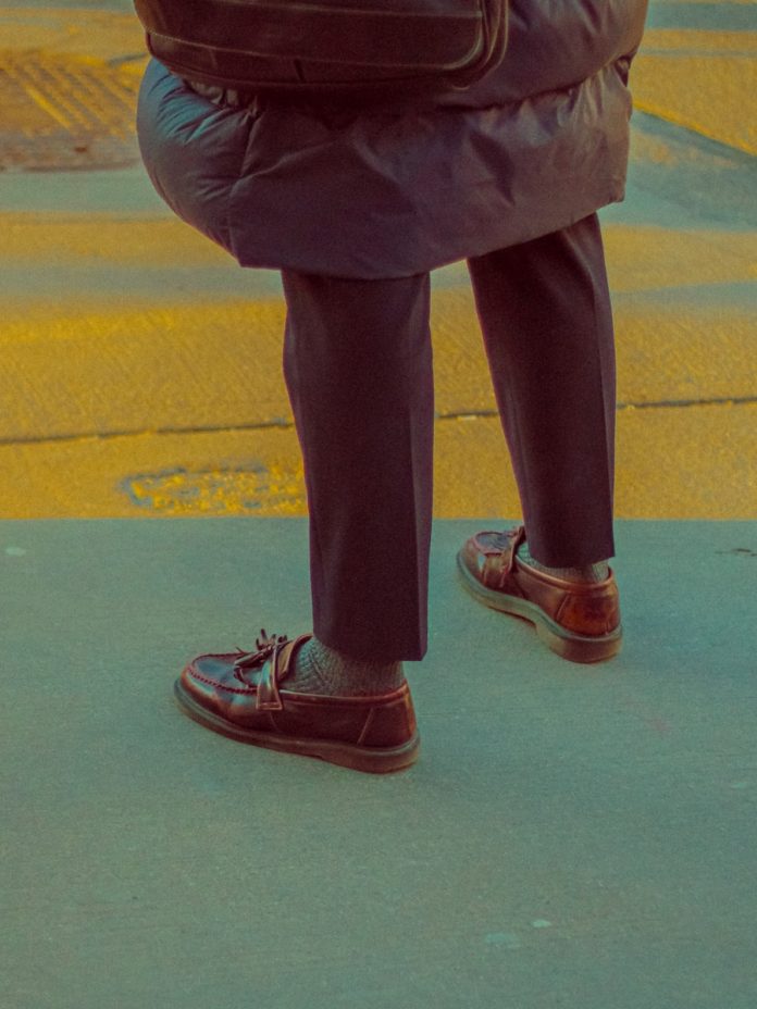 Person wearing brown loafers walks on a crosswalk.